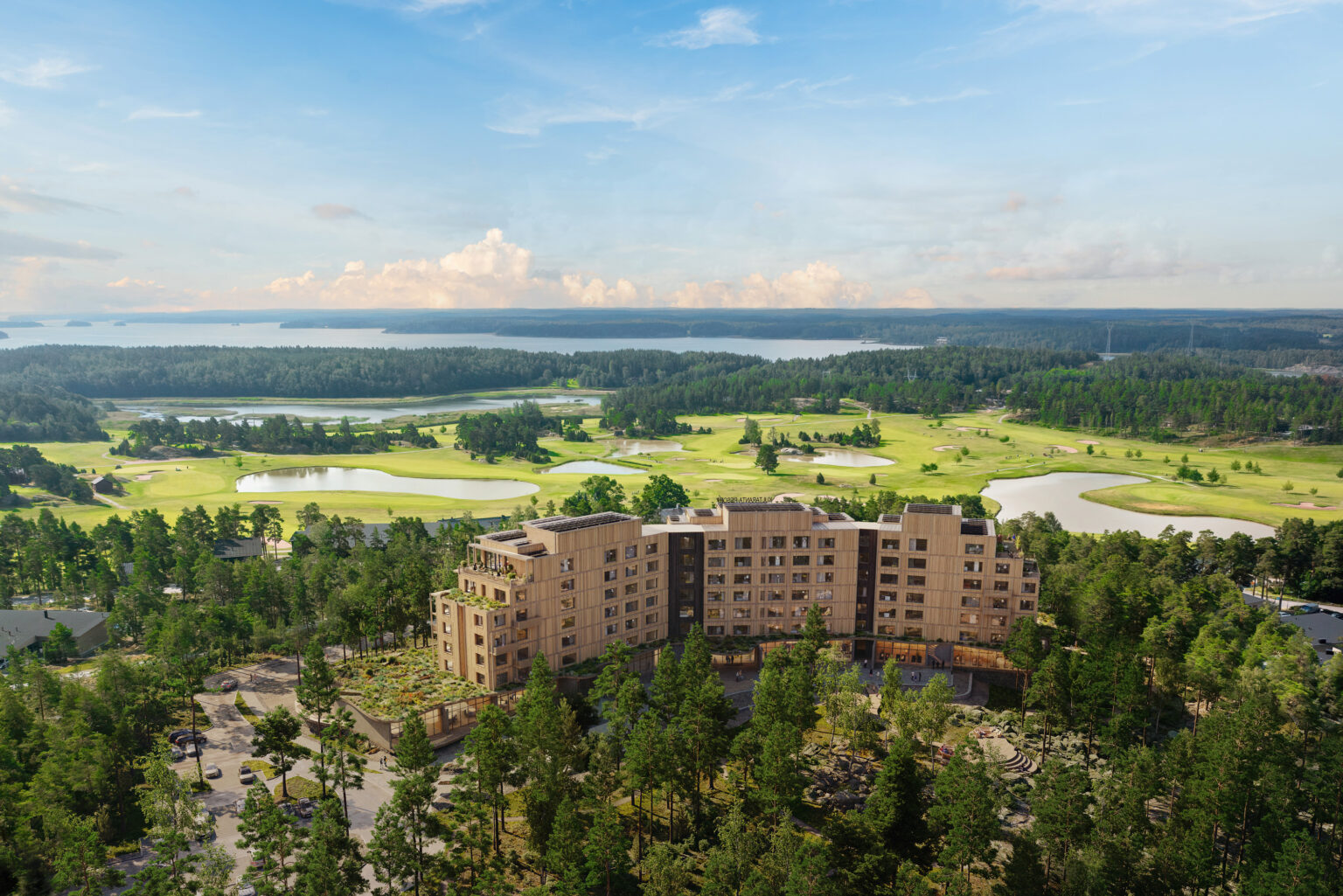 Havainnekuva uudesta hotellista ilmasta käsin, taustalla näkyvät golfkentät. Hotelli on hieman kaartuvat ja pitkänomainen.
